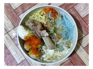 Bakso. A bowl of rib meatballs with yellow noodles, blue vermicelli, shredded cabbage, fried onions and chili sauce on a wooden patterned table. The meatballs look very delicious and delicious.