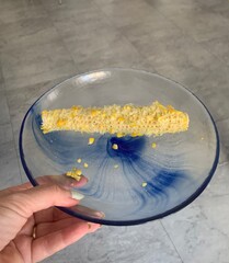Woman holding a corn on the cob with kernels removed on a glass plate