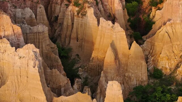 Drone view of eroded sandstone pillars lit by golden sunlight in Yuanmou Earth Forest, Yunnan, China