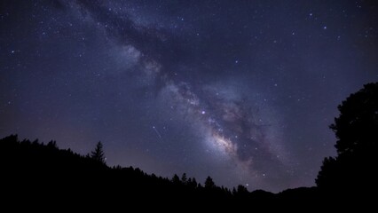 Fototapeta premium Stunning Milky Way galaxy stretches across a clear night sky over silhouetted trees and hills