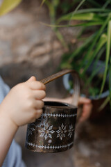 Child watering plants from a watering can. Green garden, greenhouse, summer