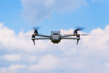 Modern quadcopter hovering against backdrop of blue sky with scattered clouds