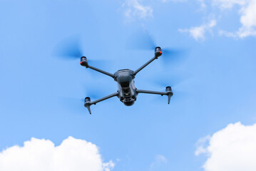 Bottom view of a flying drone with spinning propellers against blue sky and clouds