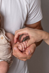 A newborn's hand is attached to the thumb of the mother's hand and supported by the father's hand