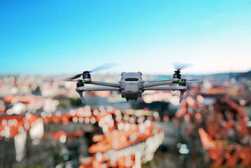 Modern quadcopter flying above cityscape with red rooftops and clear blue sky