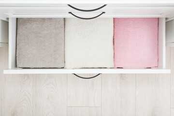 Folded colorful soft terry towels in white drawer box at home room. Closeup. Top down view.