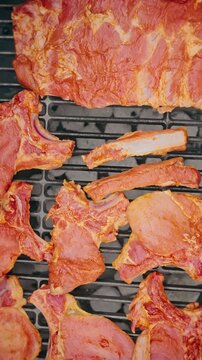 Close-up of raw marinated pork ribs placed on a barbecue grill, ready for cooking over hot charcoal.