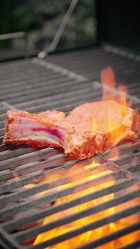 Close-up of raw pork rib cooking over bright orange flames on a barbecue grill with hot charcoal beneath.