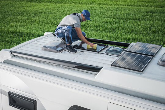 Man Performing Maintenance on Solar Panels Atop a Recreational Vehicle