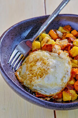 sweet potato and plantain hash topped with a fried egg, fork in bowl