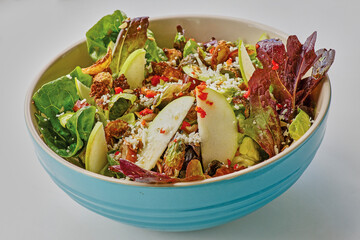 mixed green salad topped with apples, brussels sprouts, and crumbled cheese