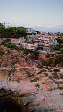 Drone video showing modern villas on rocky Spanish coastline at sunset, with clear blue sea and rugged shore in warm light.