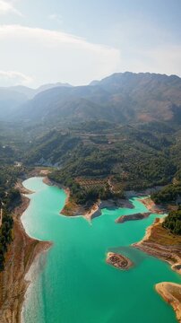 Drone video of the turquoise Guadalest Reservoir in Spain, surrounded by green hills and mountains, showing vivid water colors and scenic Mediterranean landscapes.