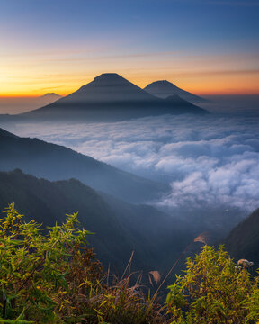 From the top of Mount Bismo Dieng Wonosobo see a stunning sunrise with pink, orange and gold hues, illuminating the landscape and revealing a stunning panorama