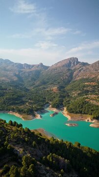 Drone video of the turquoise Guadalest Reservoir in Spain, surrounded by green hills and mountains, showing vivid water colors and scenic Mediterranean landscapes.