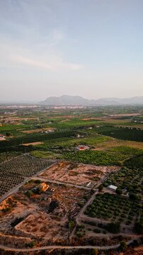 Drone video shows lush green agricultural fields with neatly arranged crops, irrigation ponds, and farm buildings under golden hour sunlight in rural Spain.