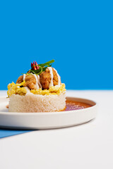 A serving of rice topped with soft scrambled eggs, crispy karaage chicken, special savory sauce, and fresh chili and scallion garnish on a minimalist white plate with a modern white & blue background.