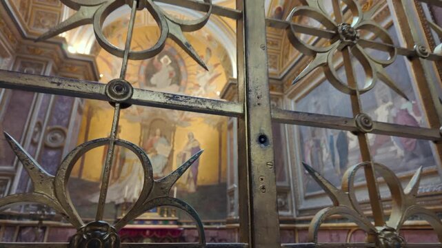View through decorative iron gate into basilica apse with golden fresco of Virgin Mary, saints, and surrounding marble architecture