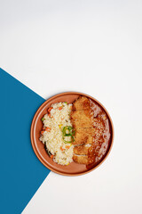 Top view of crispy chicken katsu served with curry sauce and vegetable fried rice on a brown ceramic plate, isolated on white and blue background, Asian Japanese fusion cuisine concept.