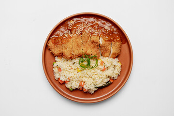 Top view of crispy chicken katsu served with curry sauce and vegetable fried rice on a brown ceramic plate, isolated on white background, Asian Japanese fusion cuisine concept.