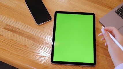 Person is writing on a green tablet. A phone and a laptop are also on the table