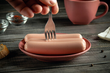 Hand holds a fork, poised to pierce soft sausages resting in a pink plate. A warm, inviting...