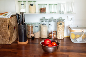 Kitchen countertop with a bowl of fresh tomatoes, shelves nearby holding jars and food containers, warm and inviting cooking space.