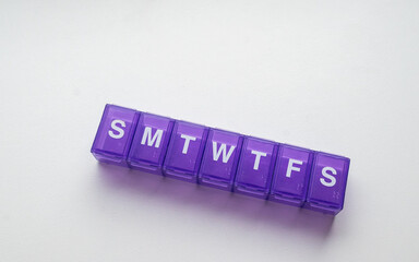 Purple weekly pill organizer with separate compartments for each day, isolated on a white...