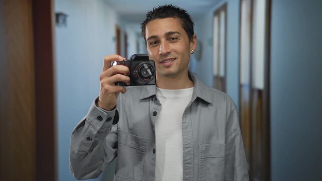 Young man photographing himself with camera in hotel hallway, capturing indoor hotel environment highlighting personal moments and creativity in a casual setting.
