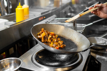 Chef stir-frying vegetables and meat in a wok with rising steam in a professional kitchen,...