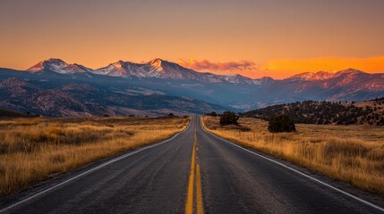 Fototapeta premium Scenic road leading to majestic mountains under a vibrant sunset sky, offering a breathtaking view of nature's beauty.