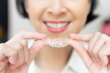 Transparent dental aligners displayed in focus by a smiling woman, symbolizing modern dental care.