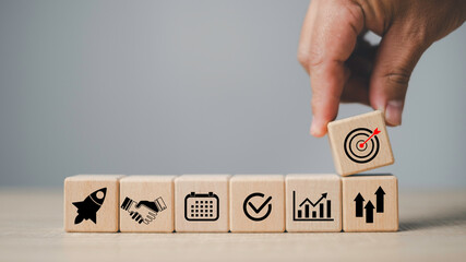 Wooden blocks with business icons including rocket, handshake, calendar, check mark, growth chart, and target, symbolizing startup launch, business target, planning, partnership, and success concept.