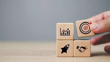 Wooden blocks with business icons showing growth chart, target, rocket, and handshake, representing business target, startup launch, partnership, and success concept with copy space.