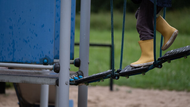 Fototapeta Child wearing bright yellow rubber boots walking across a rope bridge on a playground