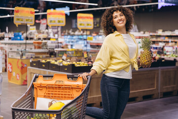 Woman Choosing Pineapple in Supermarket Holding Shopping Cart
