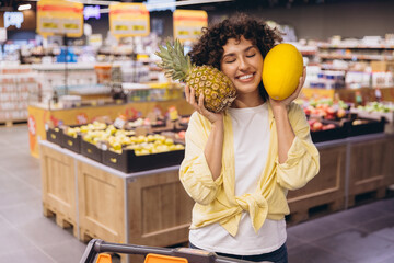 Happy customer holding pineapple and melon in supermarket
