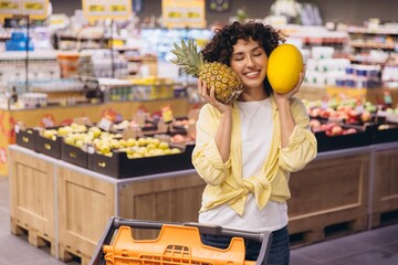 Woman holding pineapple and melon enjoying grocery shopping at supermarket