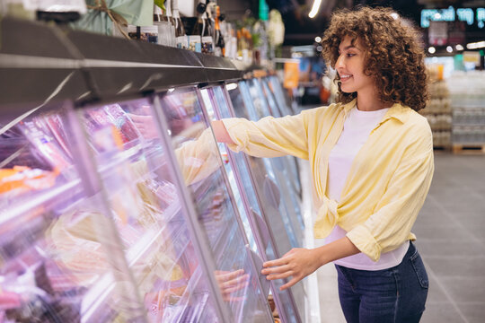 Woman choosing groceries from refrigerated shelves in supermarket