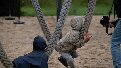 Child on large rope swing being photographed at playground