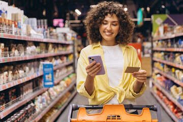 Young Woman Using Smartphone and Credit Card While Shopping in Supermarket