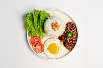 Top view of cumin-spiced beef served with steamed white rice, sunny side up egg, fresh lettuce, and tomato slices on a white plate, photographed on a clean white background.