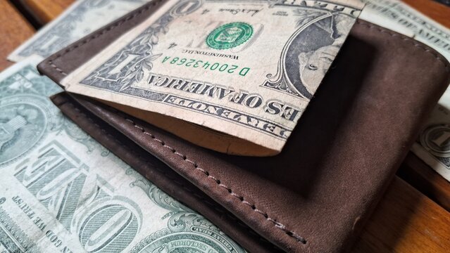 Dollar bill on top of leather wallet on wooden background