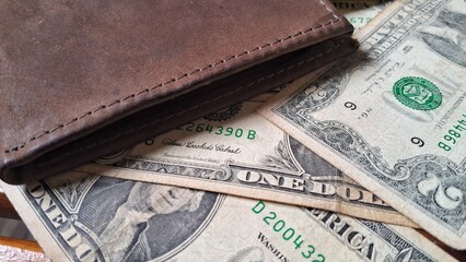 Leather wallet on top of dollar bills on a wooden background
