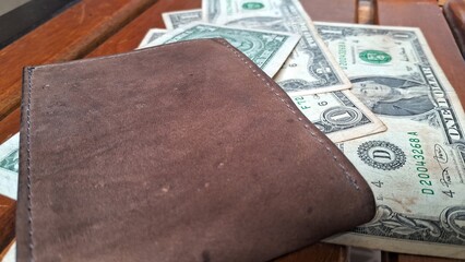 Leather wallet with a dollar bill inside on top of other dollar bills on a wooden background