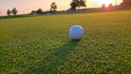 golf ballGolf ball positioned on the green in the warm glow of a sunset, with a long shadow stretching toward the camera.