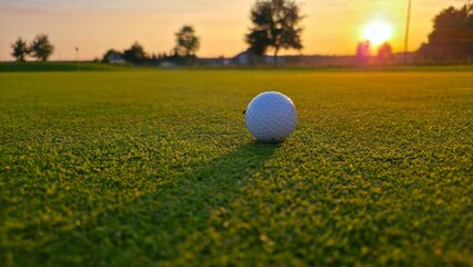 golf ball on tee Golf ball positioned on the green in the warm glow of a sunset, with a long shadow stretching toward the camera.