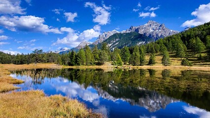 Mountain lake in autumn with view of the Swiss mountains Piz San Jon and lake reflection in golden yellow autumn colors, Lai Nair, Tarasp, Switzerland