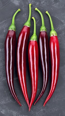 Red chili pepper with green stem on dark textured background, fresh spicy vegetable with glossy surface and vibrant color