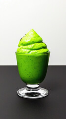 Green creamy avocado mousse dessert in clear glass on black surface with white background, fresh and smooth texture